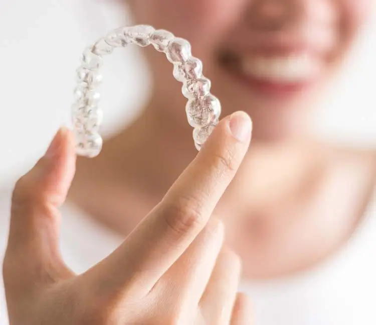 Detailaufnahme Invisalign: Zahnschiene mit der Hand in die Kamera gehalten, Hintergrund verschwommen