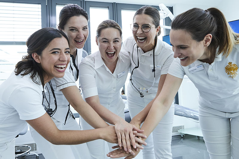 F&uuml;nf Zahn&auml;rztinnen stehen zusammen und haben Handfl&auml;chen aufeinander gelegt